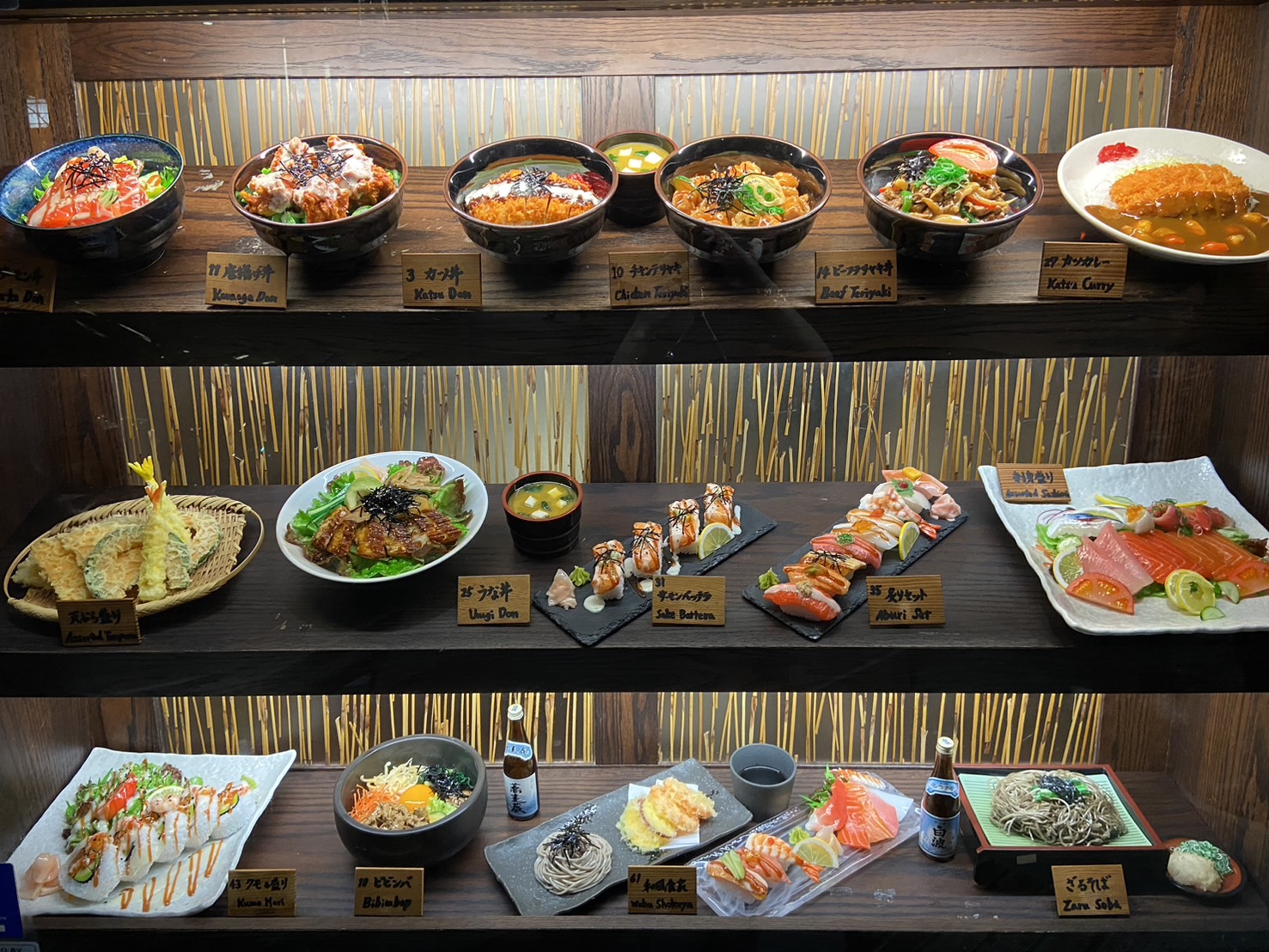 A three-shelf restaurant window display of donburi, sushi, tempura and sashimi food replicas